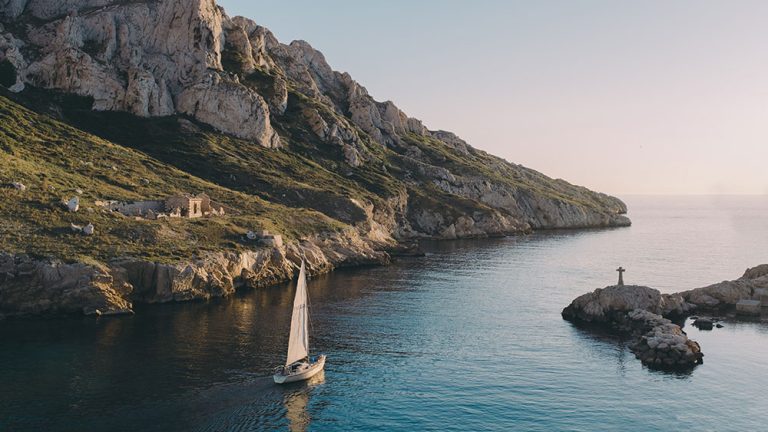 Sailboat sailing near a rocky coastline with a small cross on a rock