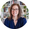 Woman with glasses smiling, in front of a bookshelf with plants